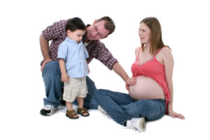 Expecting parents sitting with toddler boy over white.  Shot in studio with the Canon 20D.